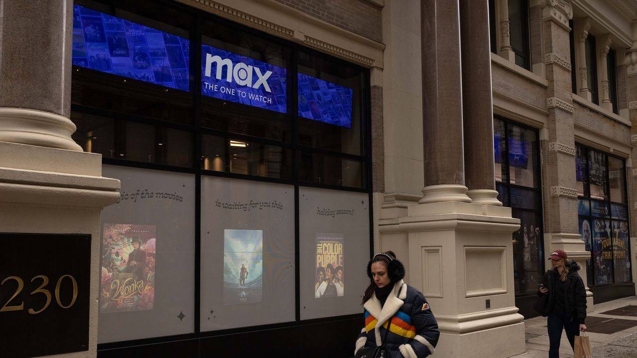 People walk past a Warner Bros Discovery building with a Max &quot;One to watch&quot; banner on the windows.