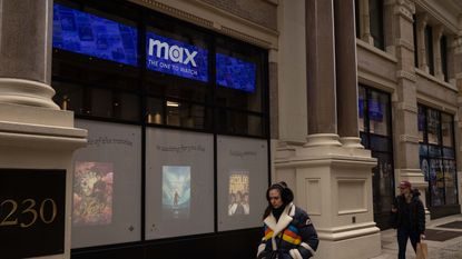 People walk past a Warner Bros Discovery building with a Max "One to watch" banner on the windows.