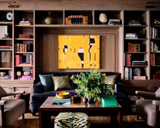 library with greige bookcase, dark blue gray velvet sofa, beige armchairs and yellow artwork