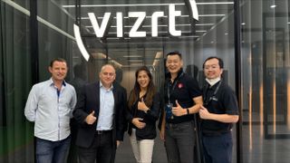 Team members from Vizrt and Midwich smile in front of the Vizrt logo after their new partnership.