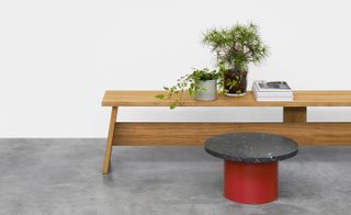 A wooden bench with pots filled with flowers is set on the far wall. In front of it is a red & gray marble side table.