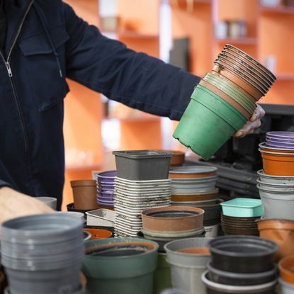 A person lifts a stack of plastic planters from a table covered in them