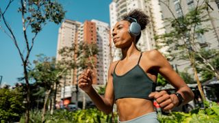 A woman in workout clothes runs in a city wearing wireless headphones.