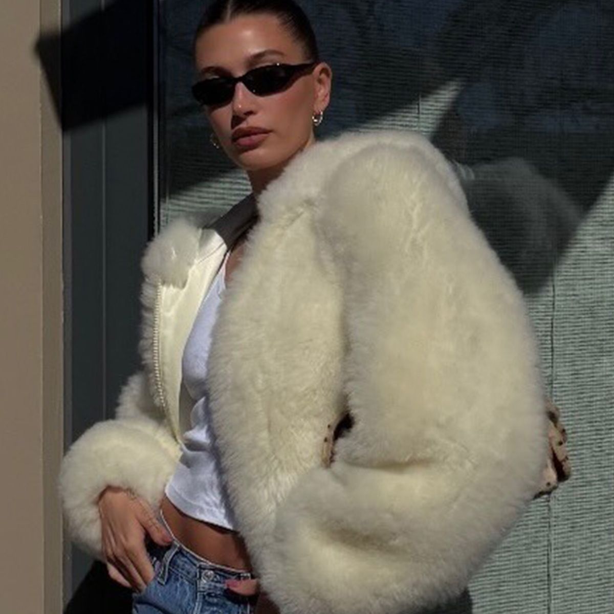 Hailey Bieber wearing a butter yellow Phoebe Philo shearling coat, a white tank top, vintage Levi's jeans, and beige heels from Jude. 