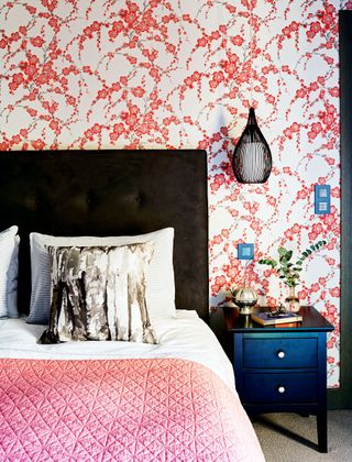 An example of black bedroom ideas showing a black bed with orange and white wallpaper