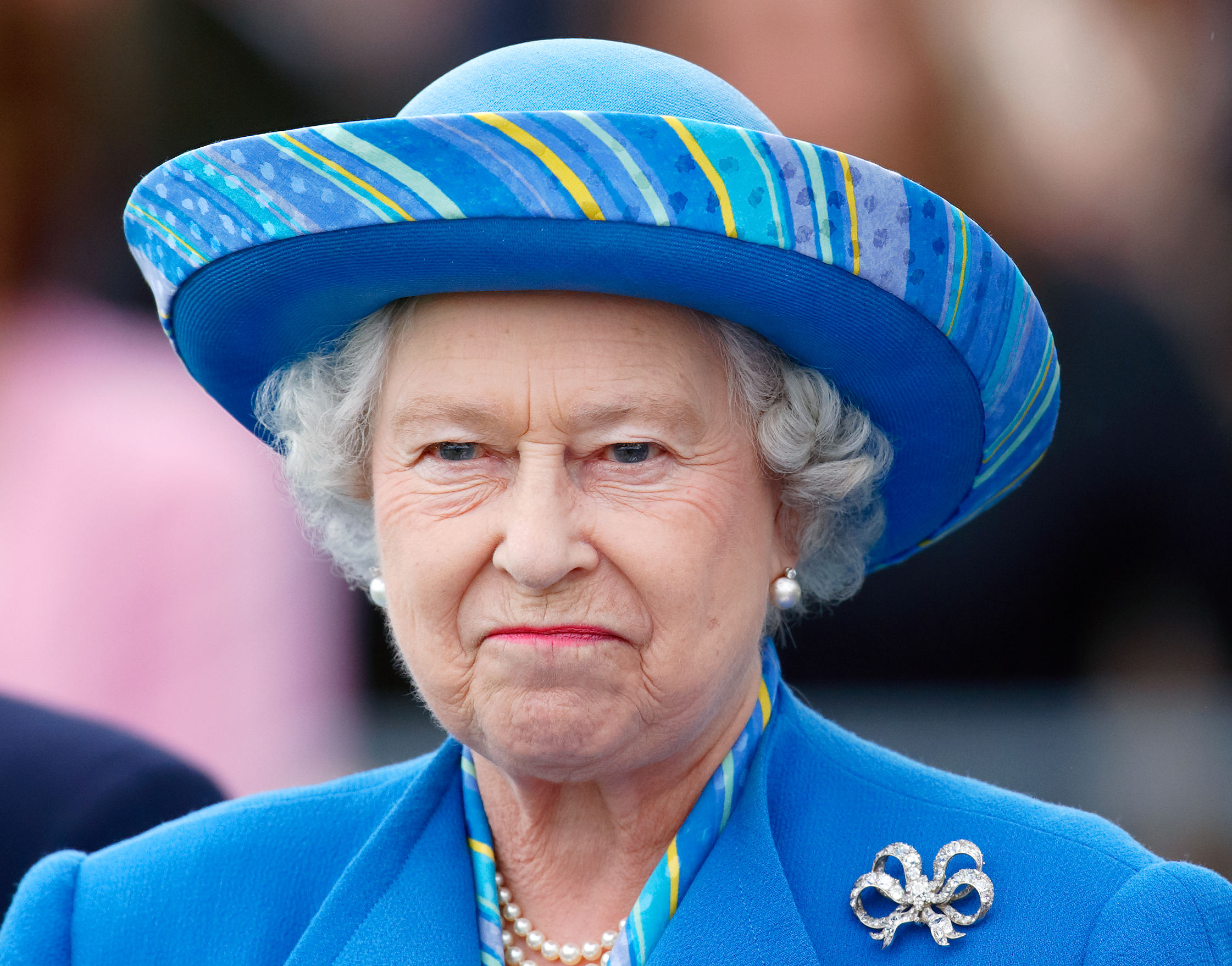 Queen Elizabeth wearing a blue hat and coat and smirking