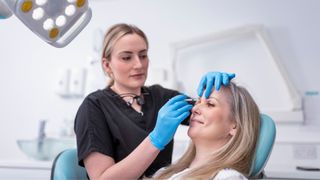 A cosmetic nurse and a female patient are pictured, as the patient receives botox treatment to her forehead