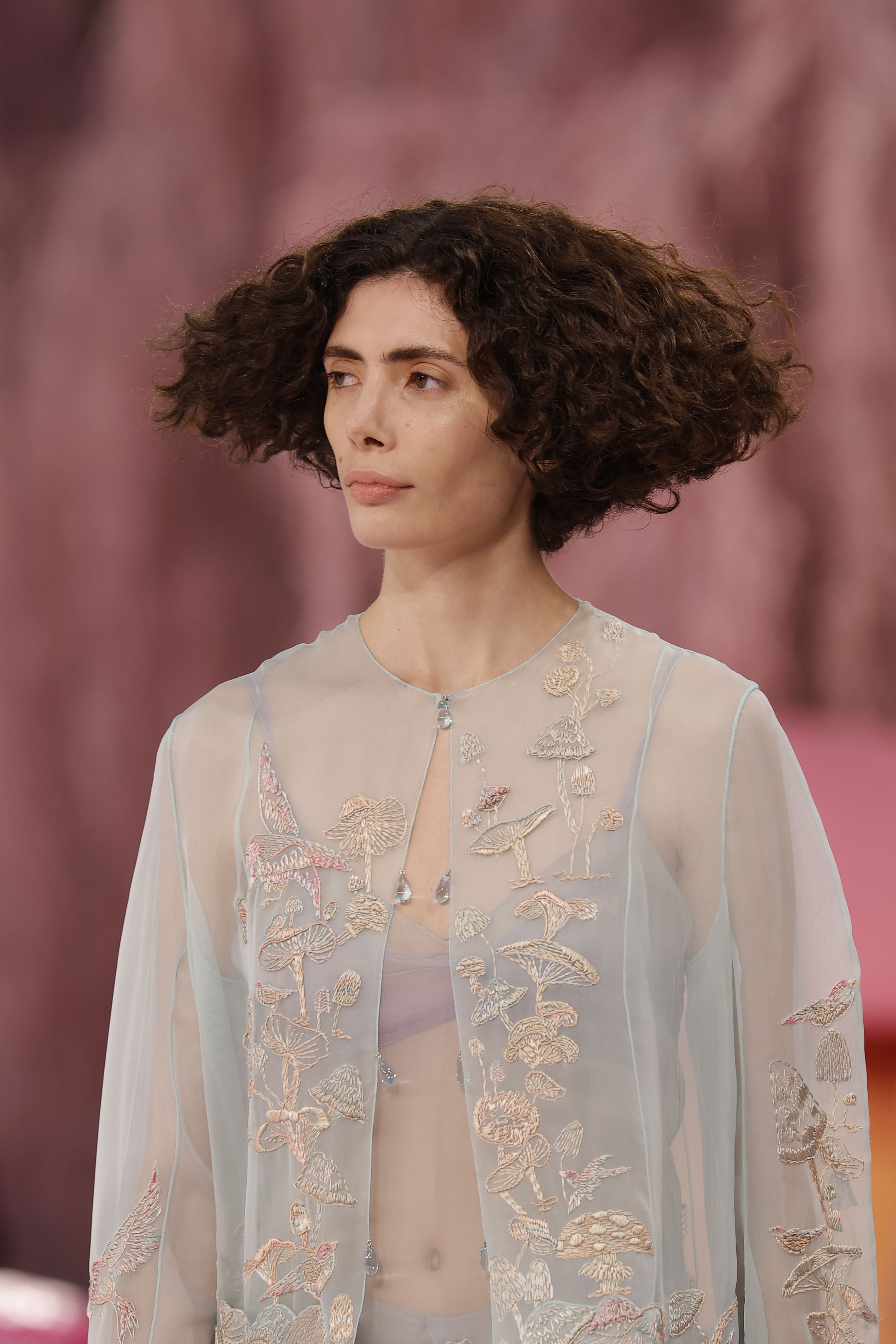 a model with short, curly hair walks the runway during couture week