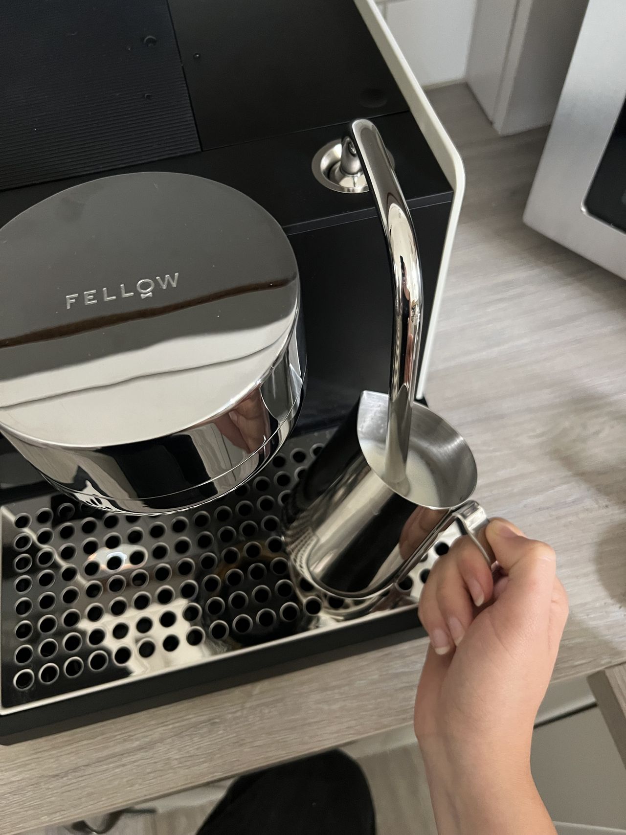 A hand frothing milk in a metal jug using the steaming wand on the Fellow series 1 espresso machine.
