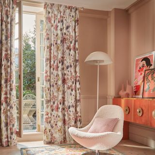 Pink room with white chair and lamp and floral curtains
