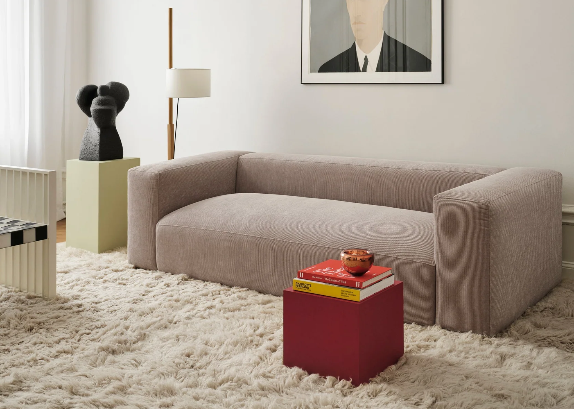 A fuzzy cream rug in a living room with a pale pink couch, a red accent table, a framed painting, and a bust