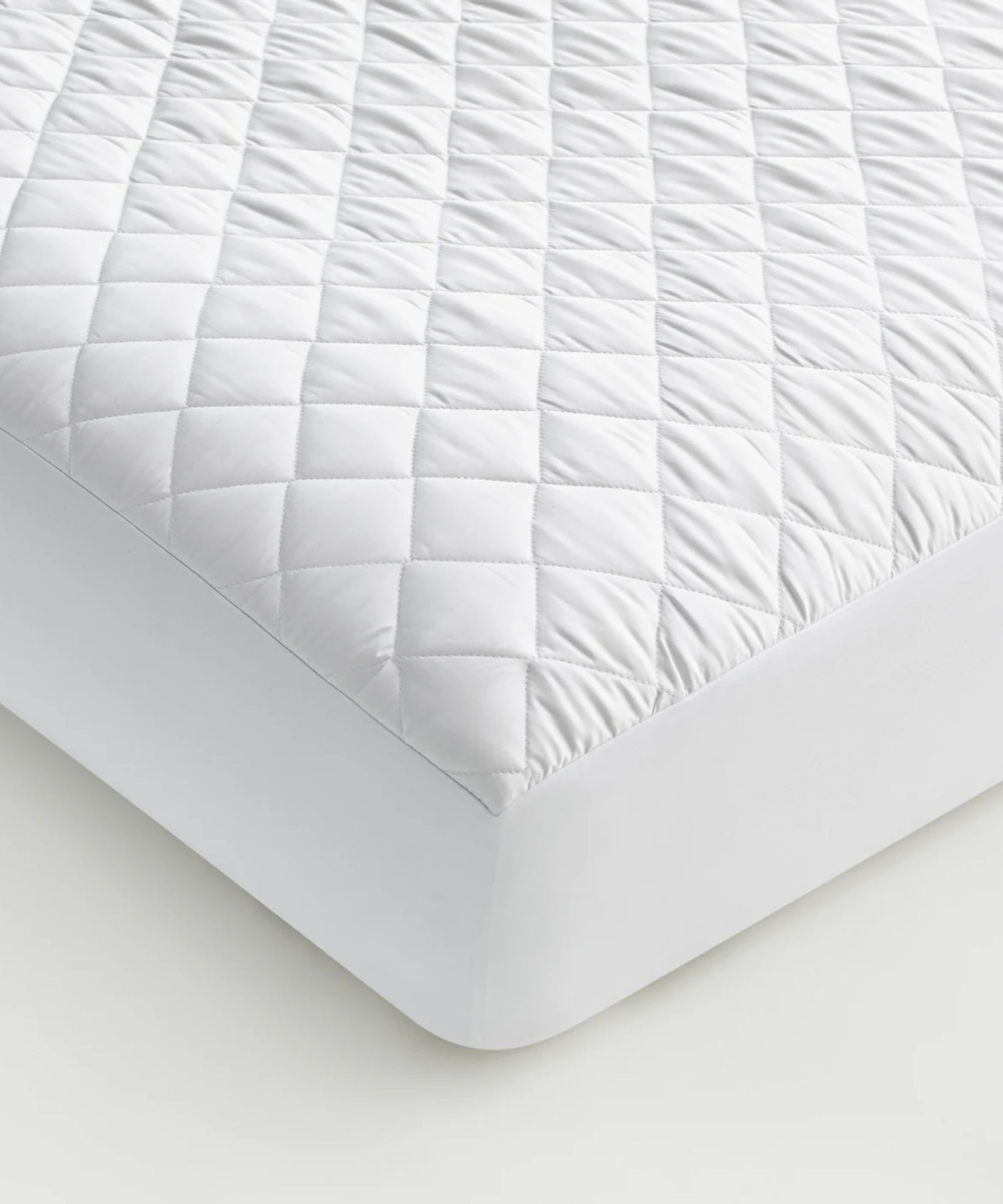 Corner of a white TempTune Cooling Mattress Pad on a mattress against a white background.