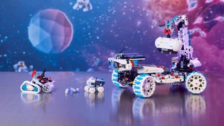 three toy models of moon rovers set against a red and blue space backdrop.