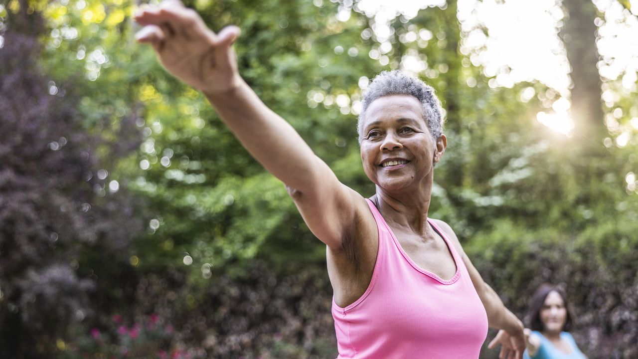 Senior woman in pink vest doing yoga pose in park