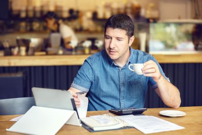A businessman drinks coffee as he goes over his books.