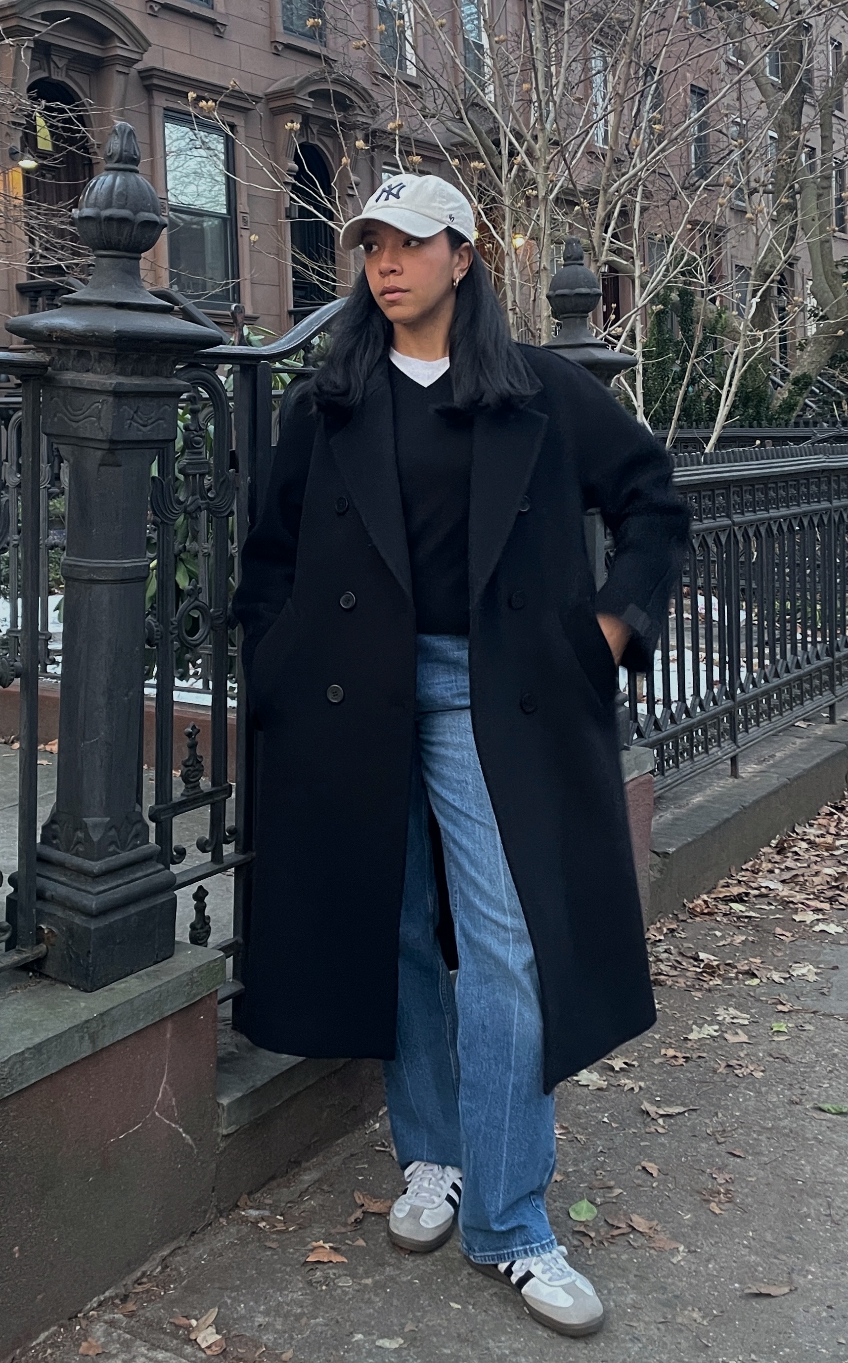 Lauren Tappan wearing a black coat, a black sweater, jeans, adidas sambas, and a cap