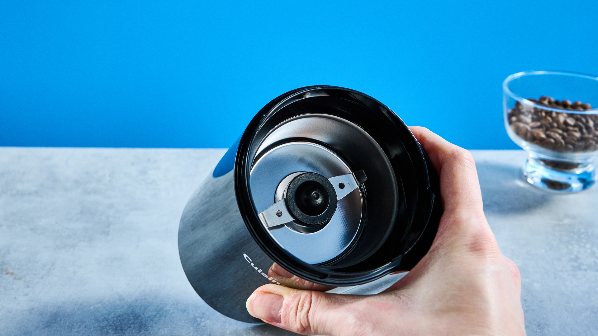 the cuisinart coffee grinder photographed against a blue background showing its blades and canister