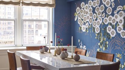 A dining room with deep blue mural wallpaper and vintage table and chairs