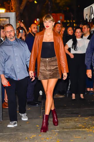 Taylor Swift walks in New York City wearing a leather jacket, mini skirt, ankle boots, and a black top