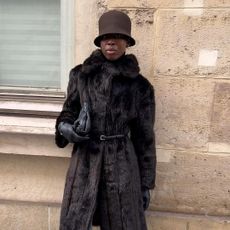 a woman wearing a wool brown bucket hat, a brown fur coat, and black leather gloves