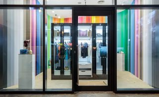 A store front with glass doors with black frames, a glass cabinet with various types of clothing inside of it and walls with vertical coloured stripes on them.