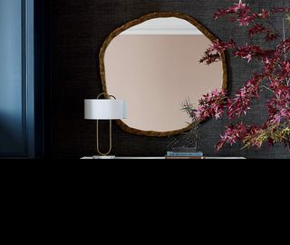 Round wall mirror hung on dark navy wall with lamp and florals