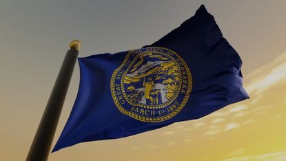picture of Nebraska state flag on flag pole against sunset in sky