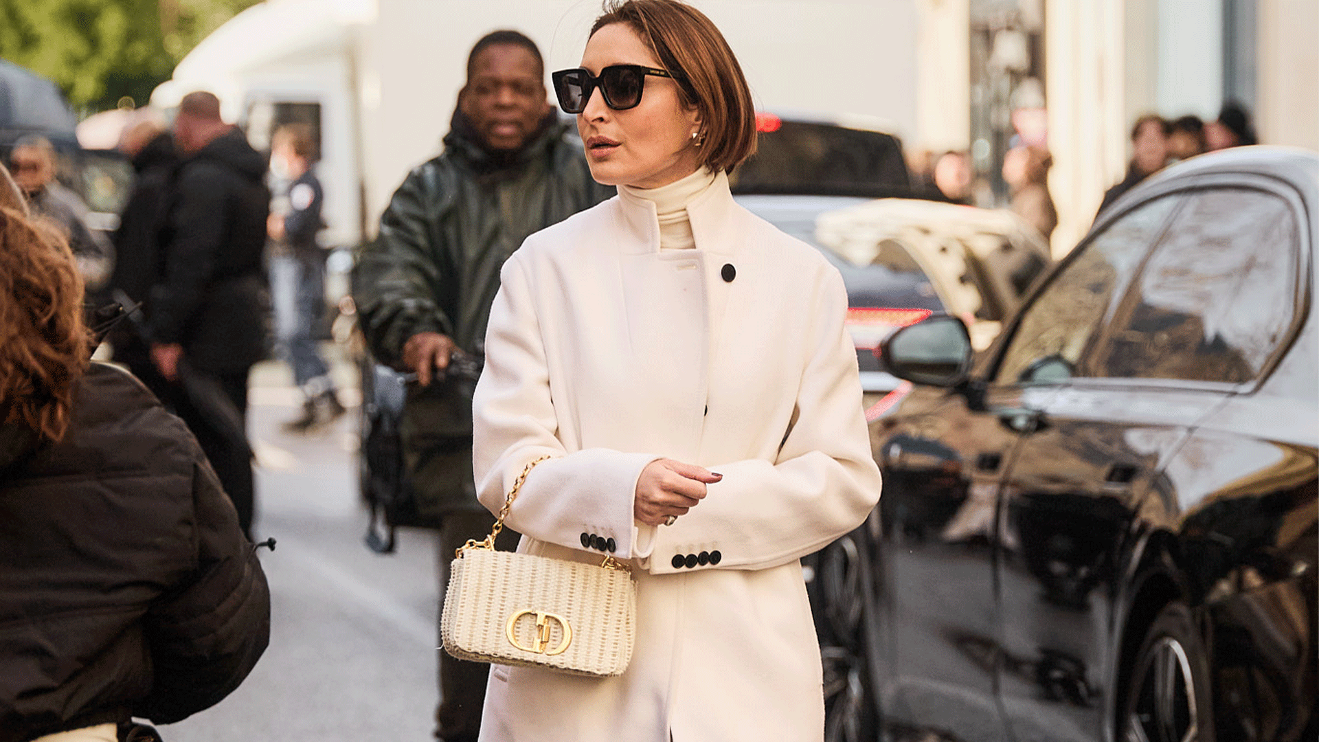 woman wears all white monochromatic outfit with white handbag and black tall boots. 