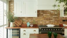 A shaker style white kitchen with wooden worktops and an exposed brick wall. A black double stove. 