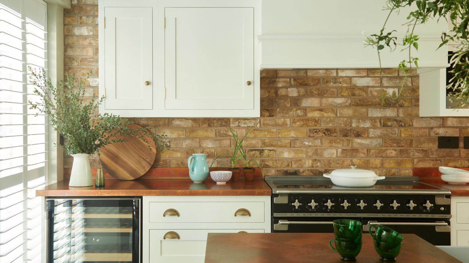 A shaker style white kitchen with wooden worktops and an exposed brick wall. A black double stove. 