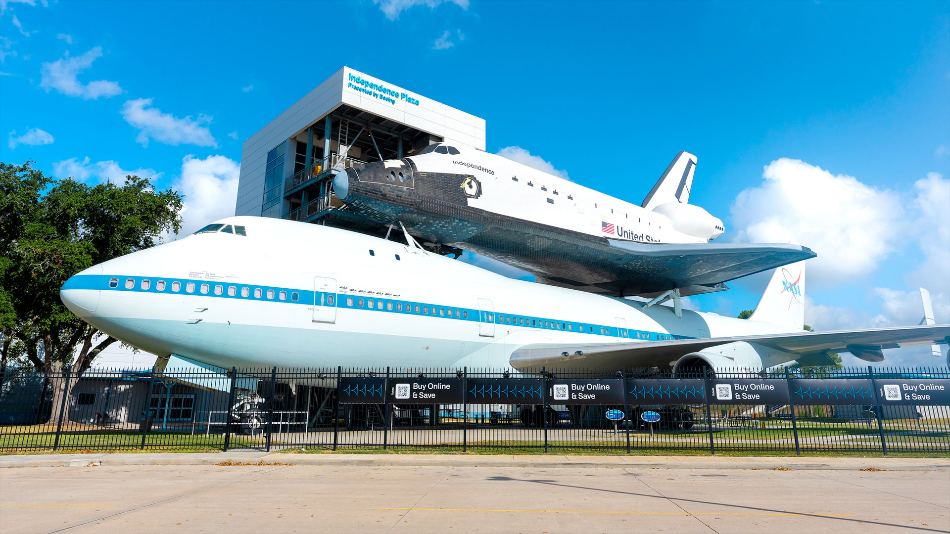 a white and black winged spacecraft mounted atop a white and blue 747 jetliner on outside museum display