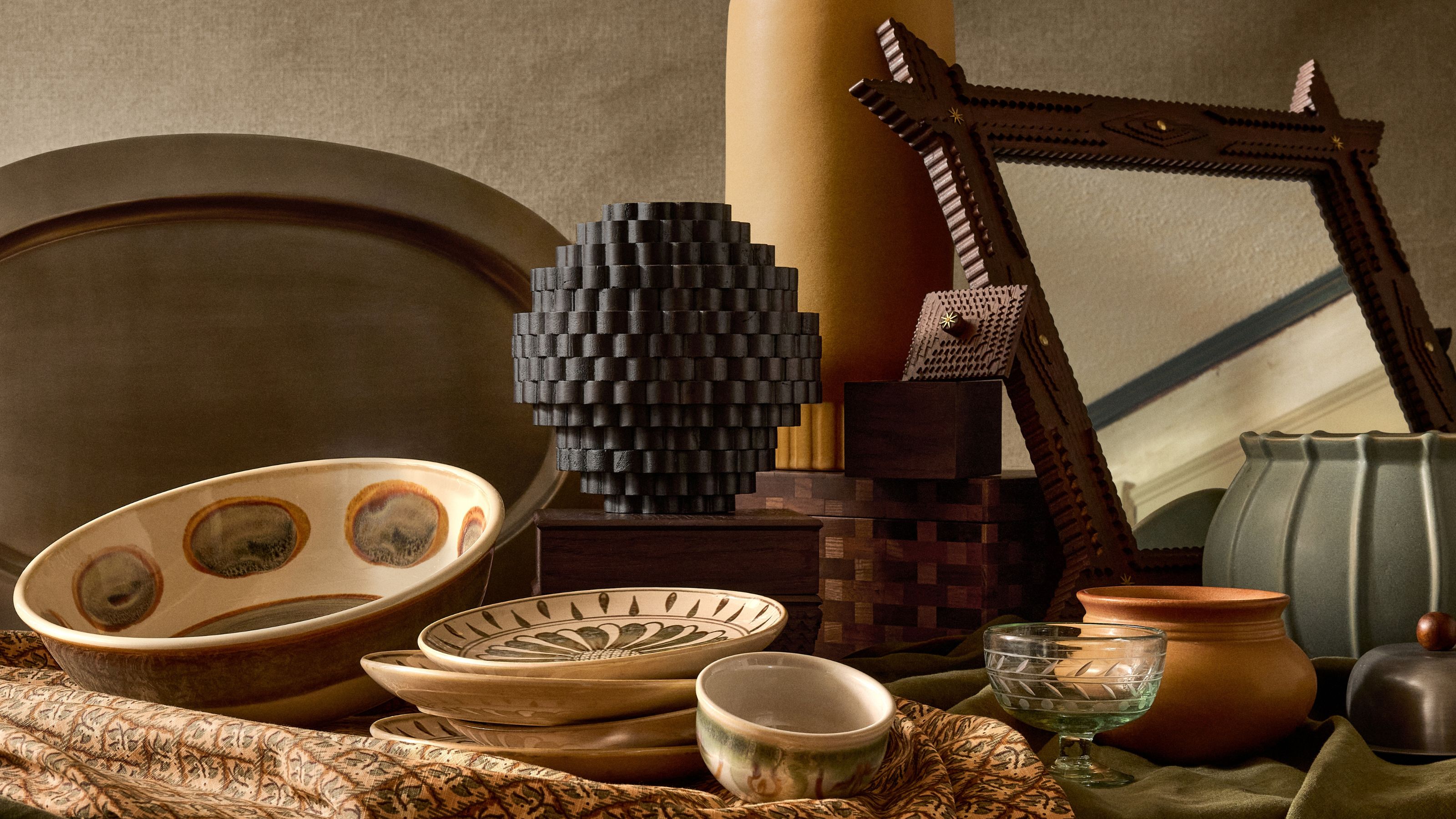 pieces from the Pierce and Ward x West Elm collection on a table including a mirror, vase, bowls and plates, and glassware