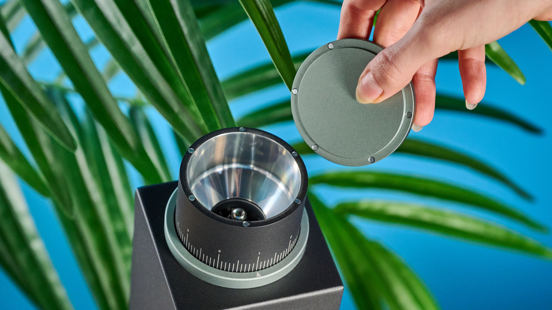 The Varia VS3 coffee grinder in use on a stone surface with a blue background