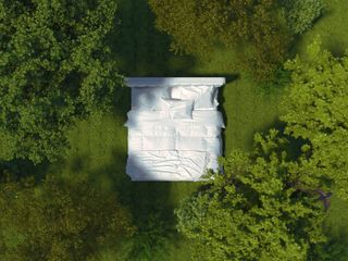 A white king size mattress outside amidst greenery and trees.