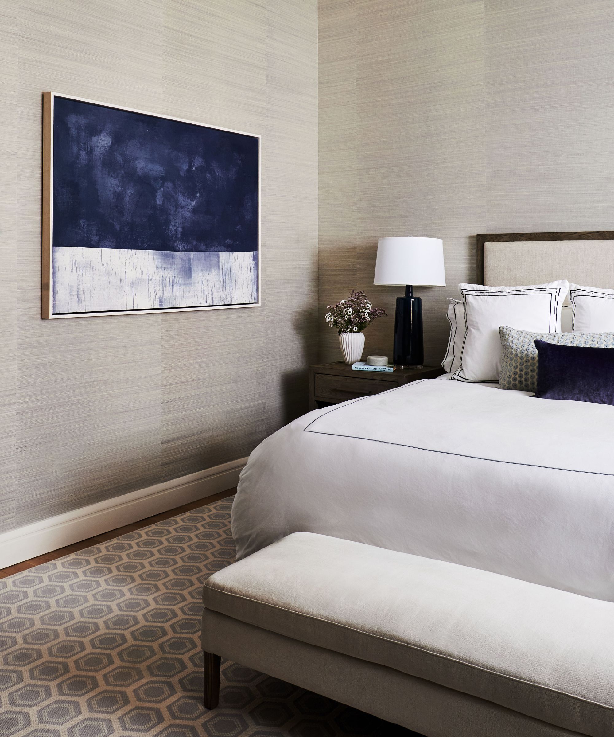 bedroom with neutral walls and dark blue cushion and artwork