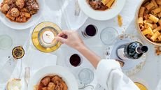 Someone lighting a candle on a dinner table with plates of pasta and meatballs, bread, and red wine