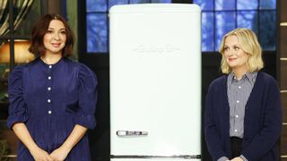Maya Rudolph and Amy Poehler standing next to an old refridgerator in Baking It season 2