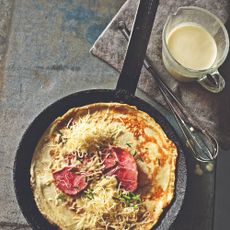 A savoury crepe in a frying pan with a jug of batter next to it