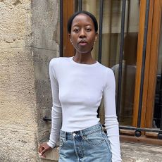 a woman wearing a white longsleeve t-shirt, blue jeans, and heels