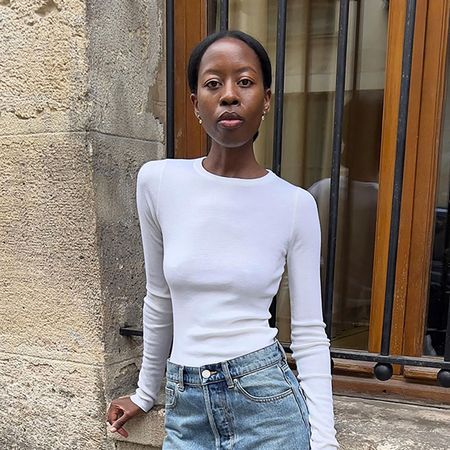 a woman wearing a white longsleeve t-shirt, blue jeans, and heels