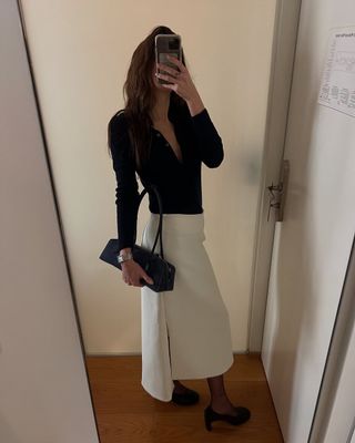 @elizagracehuber wearing black top, white skirt, and navy suede bag