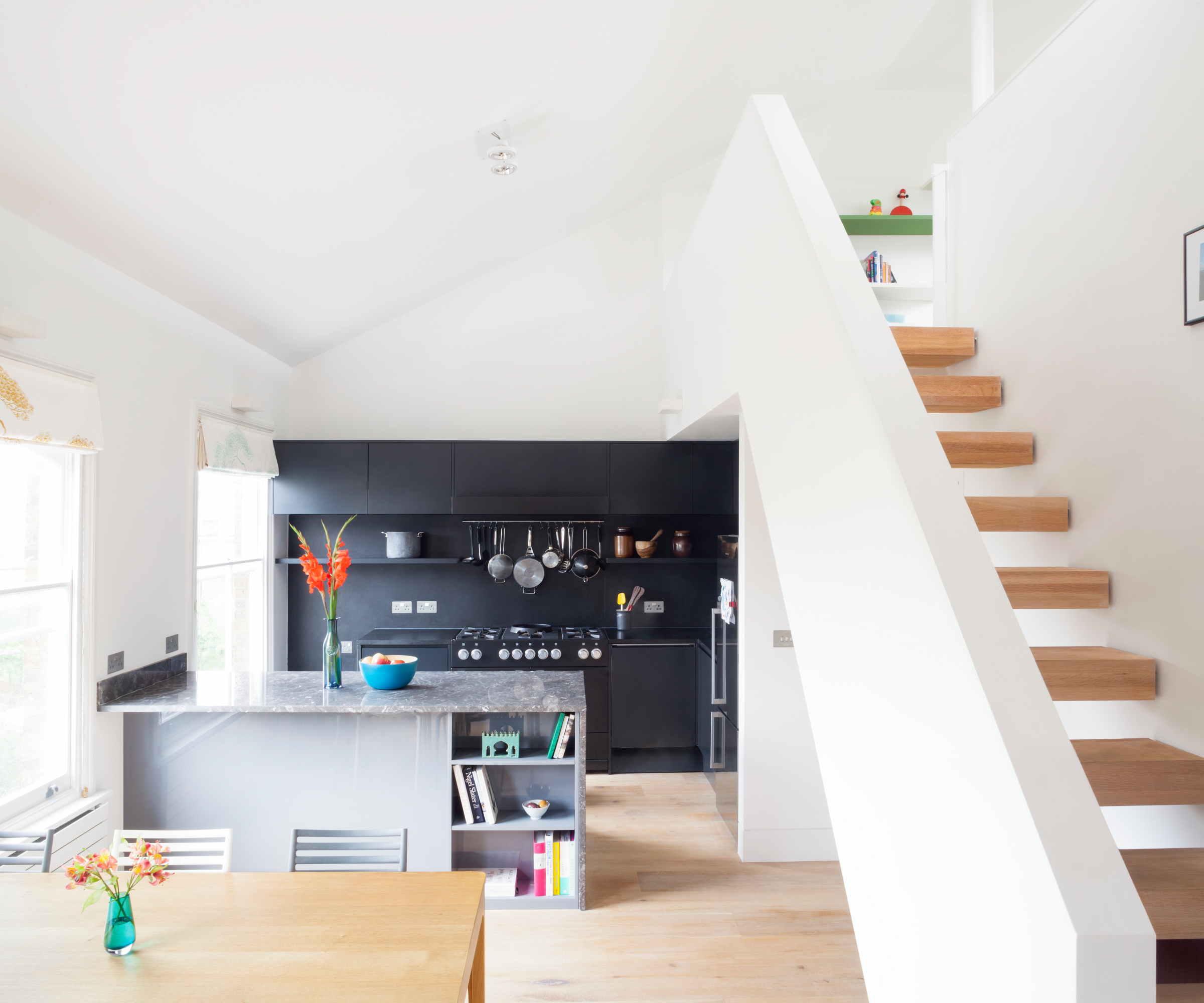 double height open plan kitchen diner painted in white with wooden floating stairs concealed behind white wall