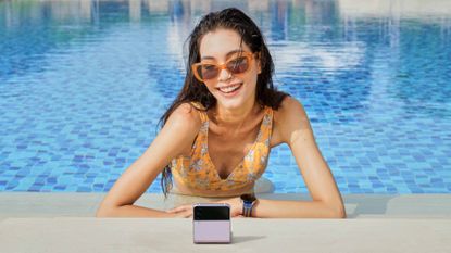 Samsung Galaxy Z Flip 4 folding phone being used by a woman in sunglasses who is partially submerged in a swimming pool