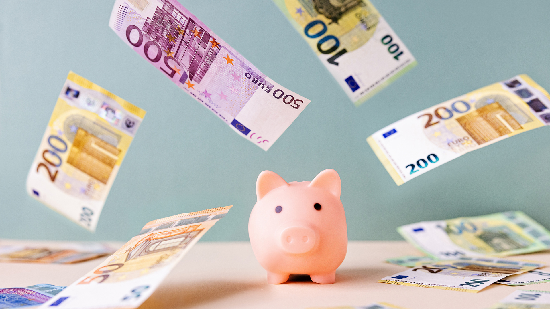 A small piggy bank surrounded by falling 100, 200 and 500 euro notes
