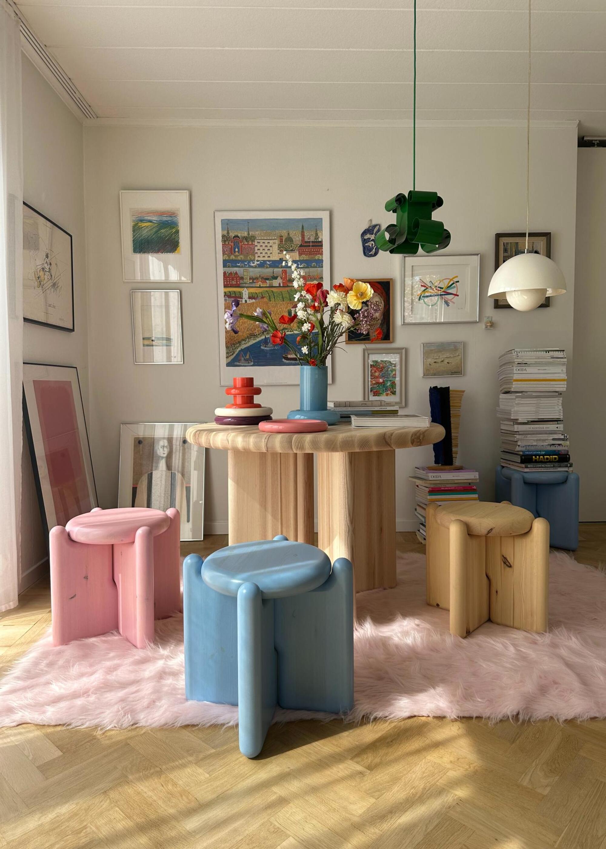 A living space with scandi-influence with a wooden table surrounded by abstract, pastel colored stools