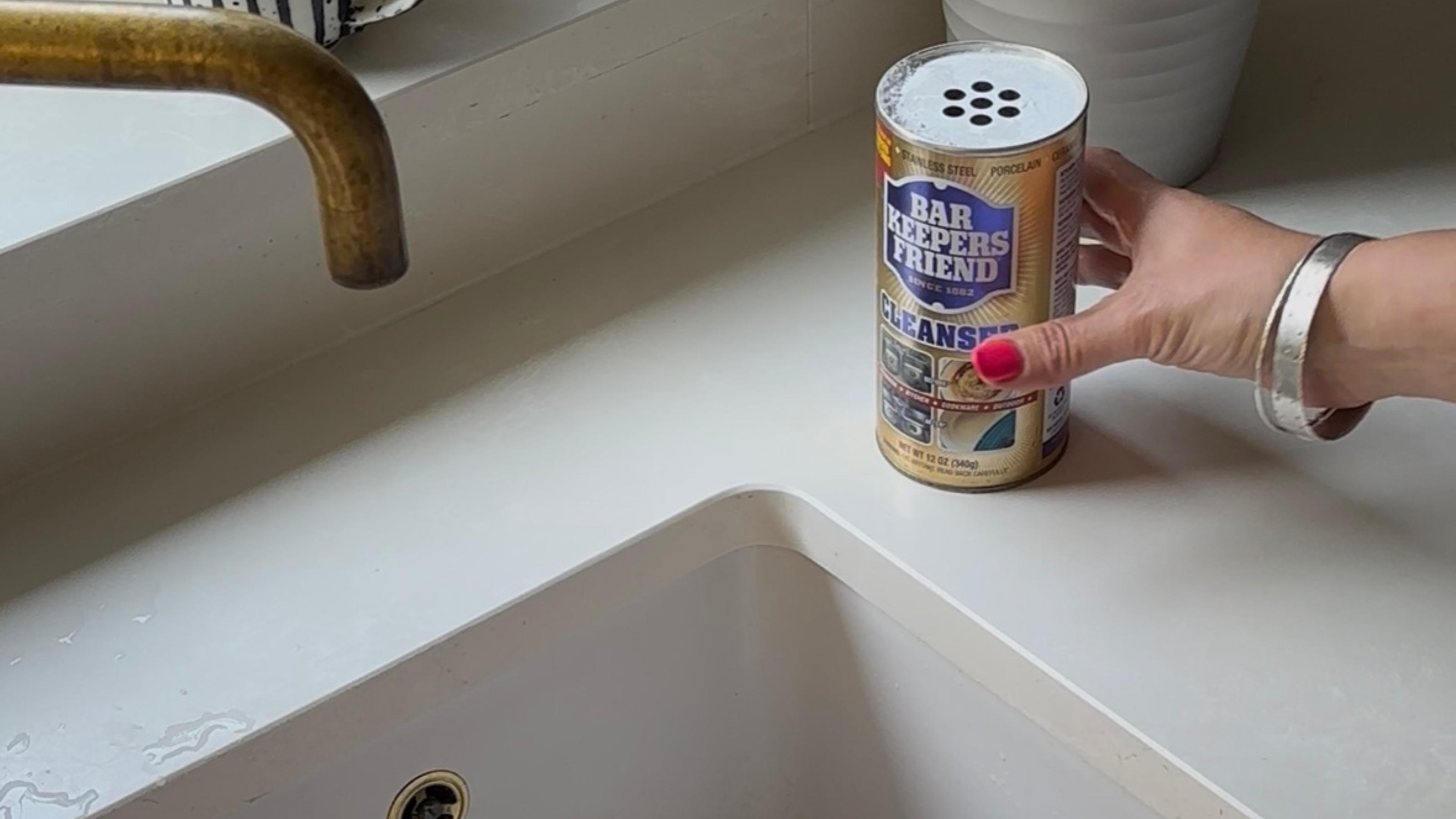 Hand placing pot of bar Keepers friend down on the side of a sink.