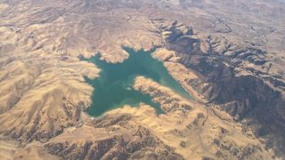 A small lake of water sits in the middle of brown mountain ridges