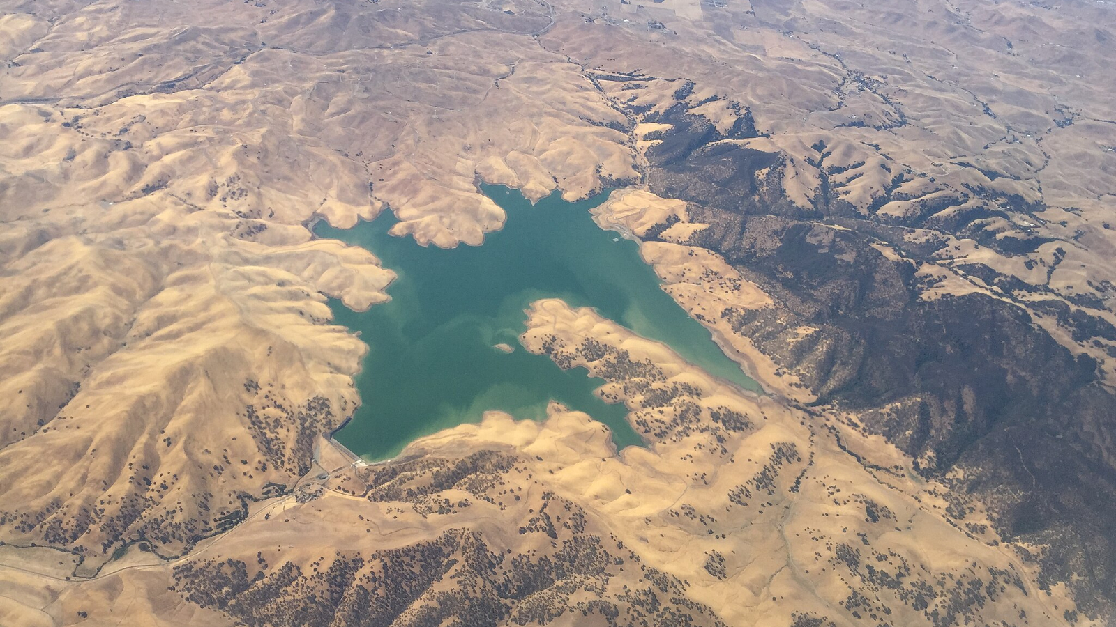 A small lake of water sits in the middle of brown mountain ridges