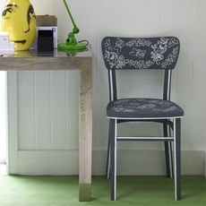 black chair with white floral design near wooden table at white wall