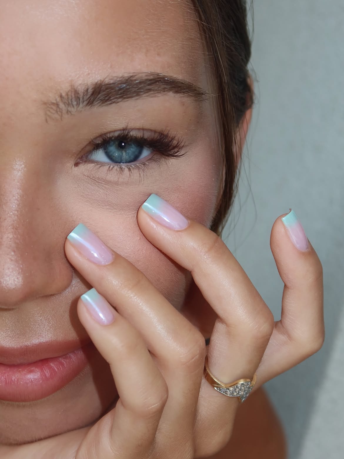 Almond-shaped nails with an opalescent base and hazy teal color diffused across the tips and a girl with bright blue eyes
